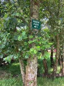 a sign for reen pier hung up on a tree