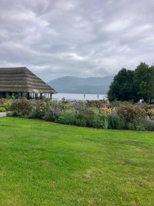 “Thatched-roof building beside a colourful flower garden overlooking a lake and mountains.”